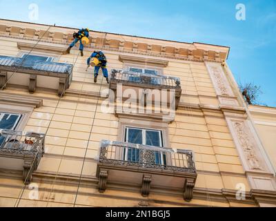 TARANTO, ITALY - OCTOBER 29, 2021: Two workers cleaning facade of historical house hanging on ropes Stock Photo