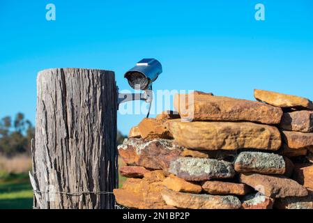 A surveillance security camera attached to a wooden gate post on a farm ...