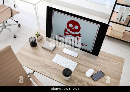 Computer with warning about virus attack on screen in office Stock Photo