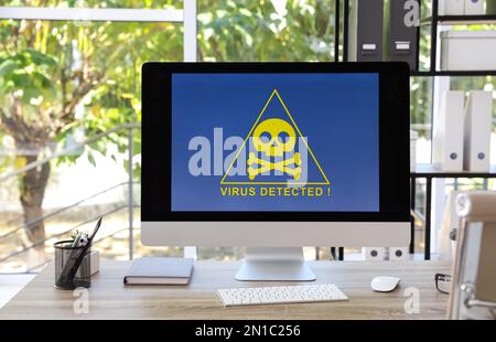 Computer with warning about virus attack on screen in office Stock Photo