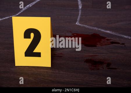 Blood stains and evidence marker near chalk outline on wooden floor. Detective investigation Stock Photo