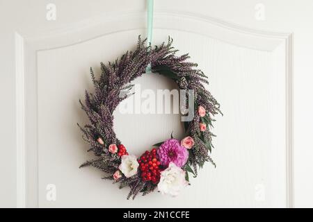 Beautiful autumnal wreath with heather flowers hanging on white wooden door. Space for text Stock Photo