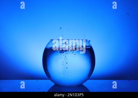 Splash of water in round fish bowl on blue background Stock Photo