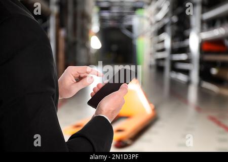 Wholesale trading. Man using WMS app on smartphone at warehouse, closeup Stock Photo
