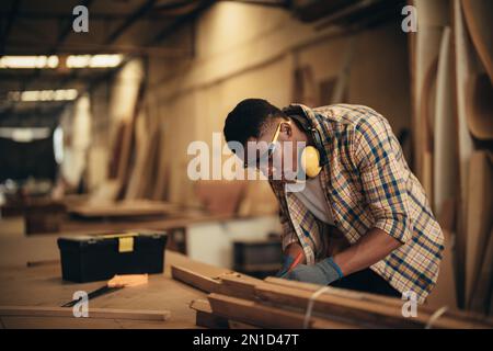 Carpenter man attend to making masterpiece woodworks handcrafted furniture fine measure in wood workshop. Stock Photo