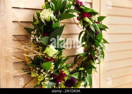 Beautiful wreath made of flowers and leaves hanging on wooden folding screen, closeup Stock Photo