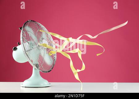 Electric fan on white table against pink background. Summer heat Stock Photo