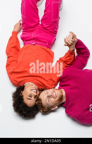 top view of pleased redhead man and curly african american woman in magenta color clothes lying on white,stock image Stock Photo