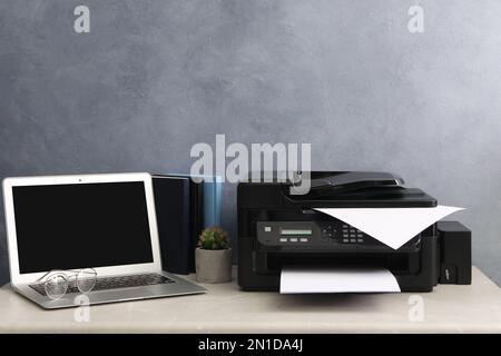 New modern printer and laptop on grey table at workplace Stock Photo