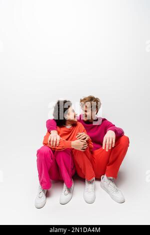 positive african american woman sitting with happy man in magenta color sweatshirt on white,stock image Stock Photo