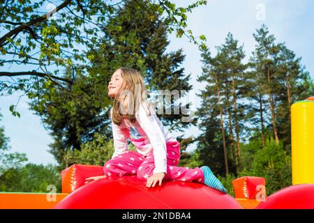Happy smiling little girl having lots of fun on a inflate castle while jumping on big balls outdoors. Stock Photo