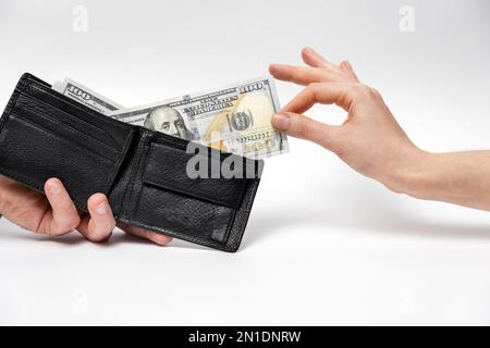 Woman's hand elegantly pulls out dollar bill from man's leather wallet. Close-up. White background. Concept of shopping, cashback and money savings. Stock Photo