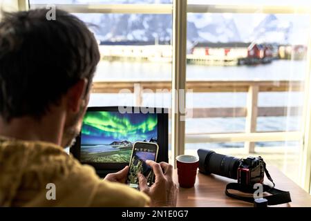 Photographer using laptop and smart phone planning the photo travels, Lofoten Islands, Norway, Scandinavia, Europe Stock Photo