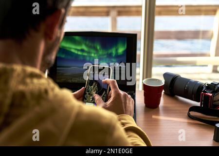 One man looking at maps on smart phone while working with laptop computer, Lofoten Islands, Norway, Scandinavia, Europe Stock Photo