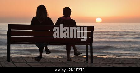 Silhouette of two women on a bench by the sea Stock Photo