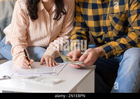 Young couple signs documents of renting or purchase real estate. Woman signing contract and man counting money. Loan and mortgage concept. Stock Photo