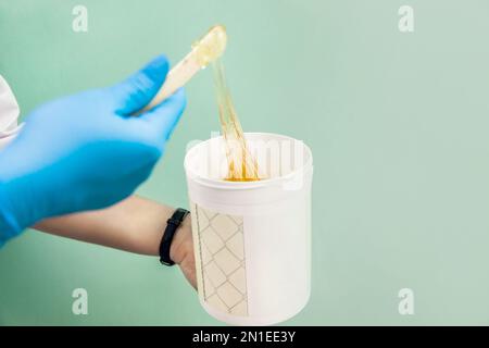 The cosmetologist holds a jar of sugar wax, shows texture of paste with a spatula. Stock Photo