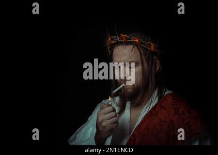 Jesus Christ smokes a cigarette wearing a crown of thorns and white chiton  toga cape himation suffering for mankind's sins in artistic mystical portra  Stock Photo