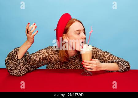 Young woman eating a cup cake with whipped cream, licking finger stock photo