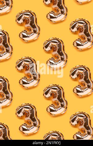 Repetitive pattern made of number 3 golden balloons. Creative layout on a yellow background. Stock Photo