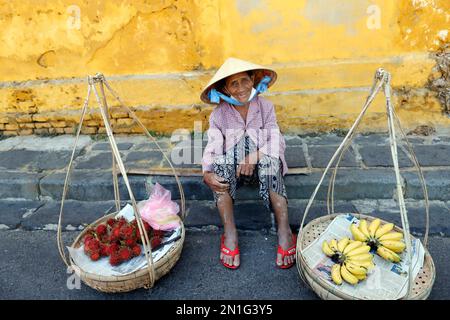 Typical street vendor with Vietnamese hat sitting down selling food, fresh fruit, Hoi An, Vietnam, Indochina, Southeast Asia, Asia Stock Photo