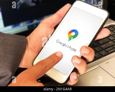 Man using Google map on mobile with laptop in the backdrop, editorial Stock Photo