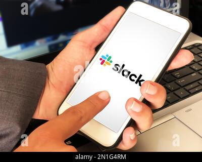 Man using instant messaging platform slack on mobile with laptop screen in the backdrop, editorial mobile app concept background Stock Photo