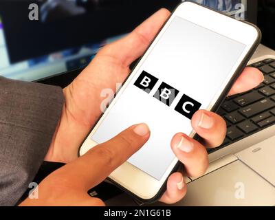 Modern BBC mobile application on screen with man touching it editorial backdrop Stock Photo