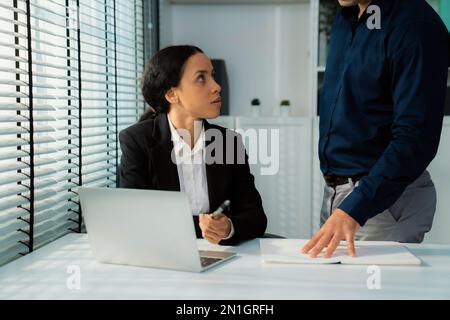 Competent female employee discussing with her colleague, employer using laptop at her office. Interpersonal relations among coworkers. Stock Photo