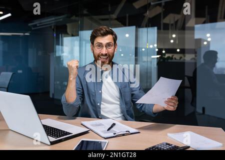 Portrait happy businessman financier, mature man with breed looking at camera and smiling, holding report with good achievement results and financial indicators celebrating victory, triumph gesture Stock Photo