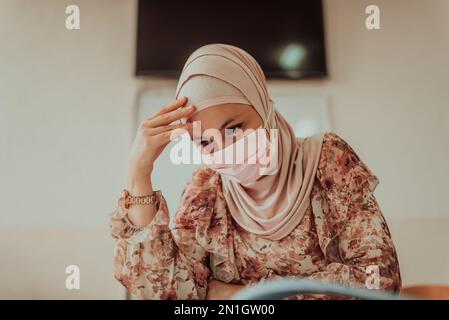 A tired Muslim teacher in a protective mask is sitting in the classroom. Selective focus Stock Photo