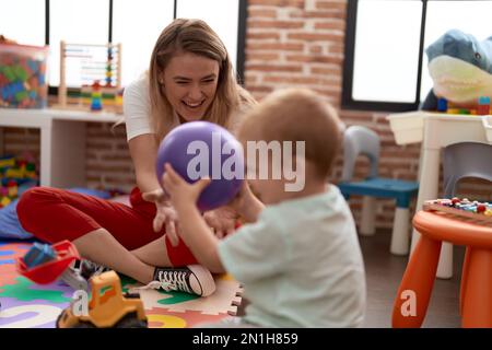 Teacher and toddler playing with ball sitting on floor at kindergarten Stock Photo