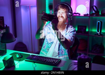 Young redhead man streamer playing video game using smartphone at gaming room Stock Photo