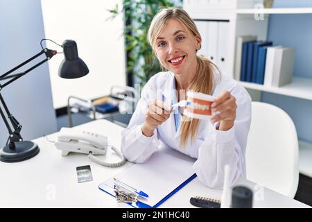 Young blonde woman wearing dentist uniform using teethbrush at clinic Stock Photo