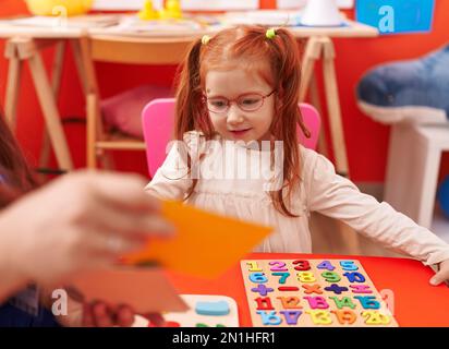 Adorable redhead girl playing with maths puzzle game sitting on table at kindergarten Stock Photo