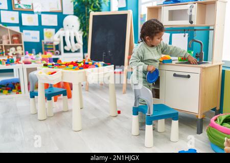 Adorable hispanic toddler playing with play kitchen standing at ...