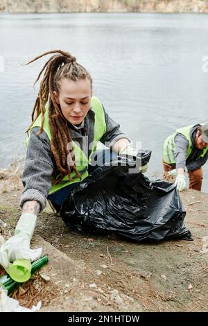 https://l450v.alamy.com/450v/2n1htdw/young-woman-with-dreadlocks-collecting-garbage-on-lakeshore-in-big-black-plastic-bag-2n1htdw.jpg