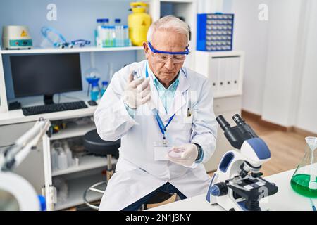 Senior man wearing scientist uniform using pipette working at laboratory Stock Photo