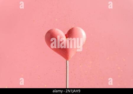 Pink Valentine's day heart shape lollipop candy on empty pastel pink background with golden flying sequins. Love Concept. Minimalism colorful style Stock Photo