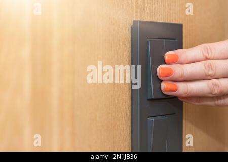 Turn on the light, a woman's hand presses the switch in the apartment close-up. Black light switch on the background of a wooden wall. The concept of Stock Photo