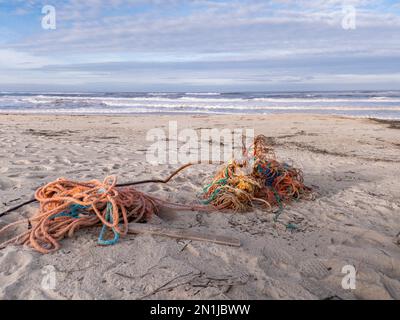 Tangled fishing boat ropes, nets and wreckage washed up on the sand of a dirty beach in Portugal with the ocean and sky in the background Stock Photo