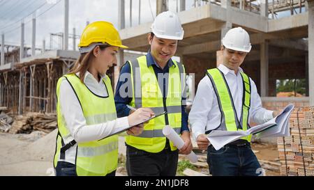 Asian Architector and engineers team with draft plan of building  talking on constructing site. Construction manager and engineer working on building Stock Photo