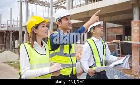 Asian Architector and engineers team with draft plan of building  talking on constructing site. Construction manager and engineer working on building Stock Photo