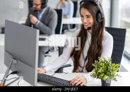 Call center worker accompanied by her team working with a headset at office. Stock Photo