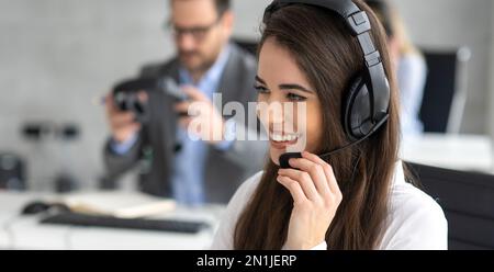 Headshot of beautiful young woman working in a call center. Friendly call center agent holding microphone while talking to customer. Stock Photo