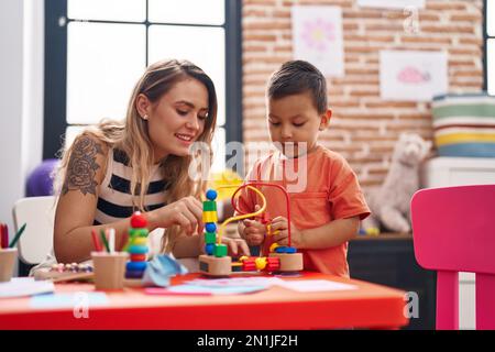 Teacher and toddler playing with toys sitting on table at kindergarten Stock Photo