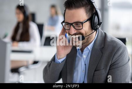 Closeup head shot of confident bearded call center operator talking and listening to customer while using headset with microphone in office Stock Photo