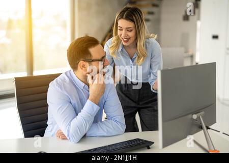 Cheerful business woman and man having conversation during meeting in front of computer at modern office. Stock Photo