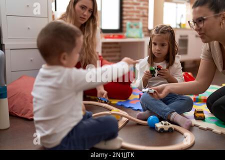 Teachers with boy and girl playing with cars toy sitting on floor at kindergarten Stock Photo