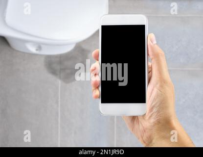 A hand holding a smartphone to call the professional to repair a water leak in the toilet Stock Photo